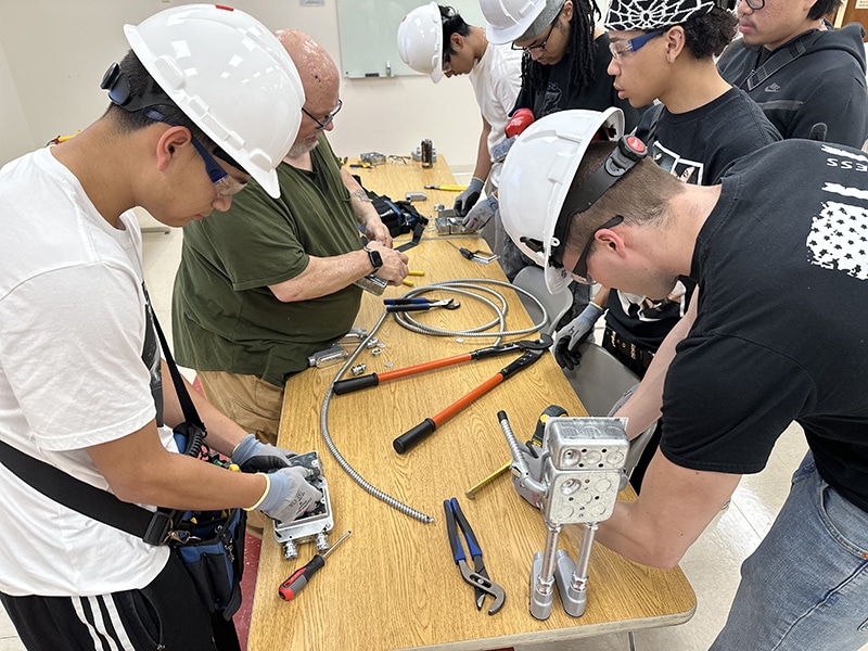Pre Apprenticeship group with hard hats working on cutting conduit